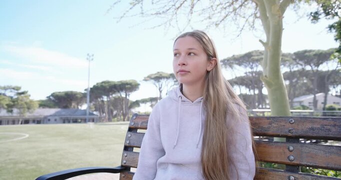 Teen female in hoodie hearing off-frame voice, turning, smiling, laughing on bench by turf field