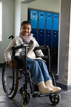 African American teenage girl sitting in manual wheelchair with coat scarf at school blue lockers