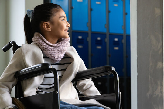 African American girl sitting in manual wheelchair wearing coat, pink scarf at school lockers