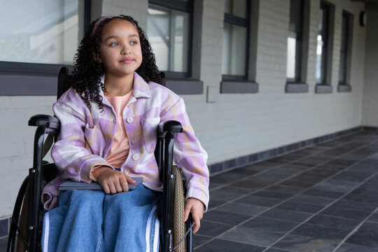 Youth African American female sitting in wheelchair holding tablet in tiled corridor, copy space