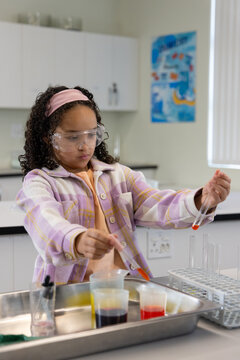African American female youth wearing goggles jacket adding red liquid with pipette in school lab