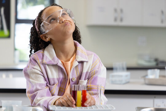 Youth African-American student sitting in school lab goggles holding rack with three test tubes