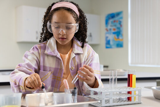 Youth African American student wearing safety goggles using pipettes and test tubes at school lab