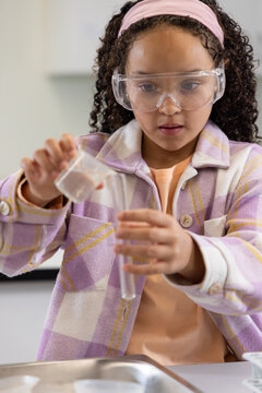 African American girl child in goggles pouring liquid from beaker into testtube on tray school-lab
