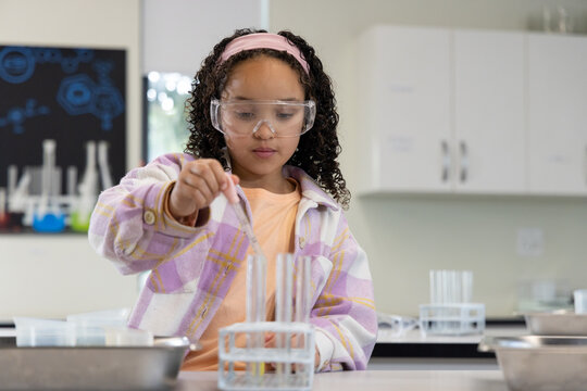 African American child standing in school lab wearing goggles holding pipette over test tubes