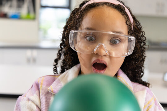 School-age African American girl wearing goggles and pink headband reacting to green balloon in lab