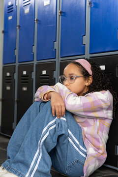 African American child curling up on tile floor by blue black lockers wearing pink headband