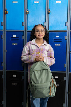 African American child standing at school lockers holding backpack wearing plaid shirt and glasses