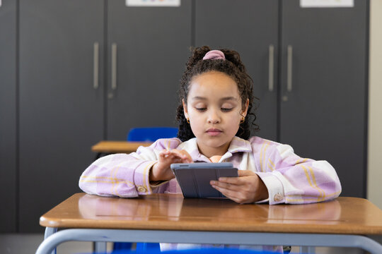 African teenage female sitting at school desk holding tablet in case wearing purple jacket