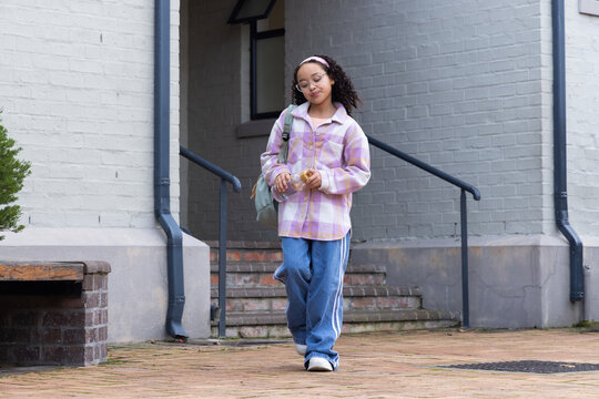 African American teen walking across brick doorway wearing plaid shacket holding bottle and pastry