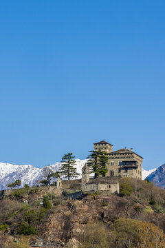 Medieval  castle Montestrutto  on a hill with snow‑capped Alps in Piedmont Italy under blue sky