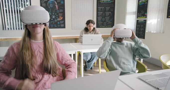 Diverse teens in lab picking up white VR headsets, learning VR while rear typing laptop headset