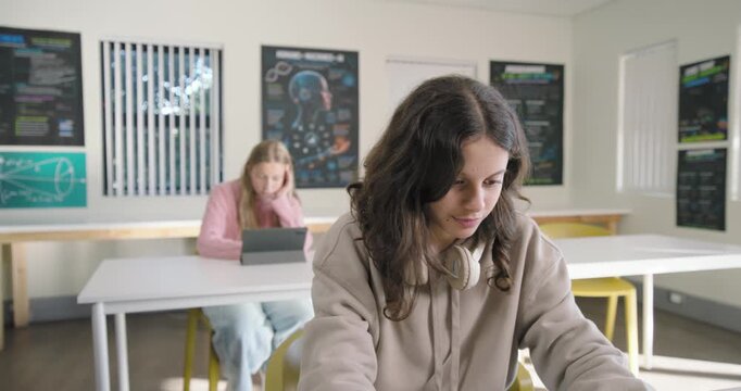 Teenage female classmates in class with front teen holding tablet, camera moving in causing smile