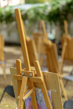 Wooden artist easel in an outdoor art class. Multiple blurred painting tripods at an open-air workshop.