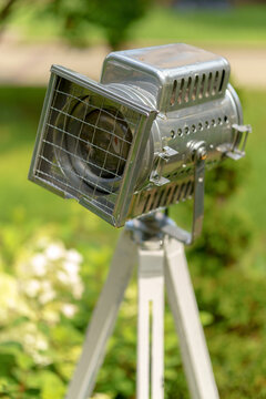 Vintage silver stage spotlight on a wooden tripod setup. Professional retro lighting equipment in an outdoor garden background.