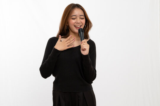 Joyful Asian female singer holding microphone performing emotional song on white backdrop