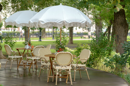 Summer restaurant veranda with retro fringed umbrellas over wooden bistro tables and wicker chairs. Open-air patio dining area with elegant garden furniture on a timber deck.