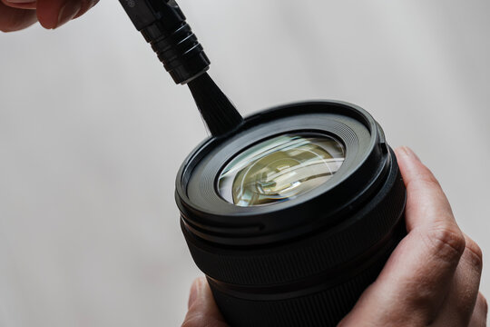 Hand cleaning camera lens with brush for maintenance