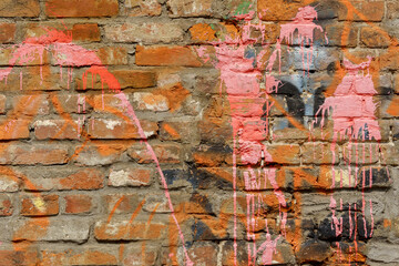 Brick wall texture with vibrant pink graffiti spray paint splatters and drips. Aged masonry background with colorful street art elements on a rough clay surface. © sandipruel