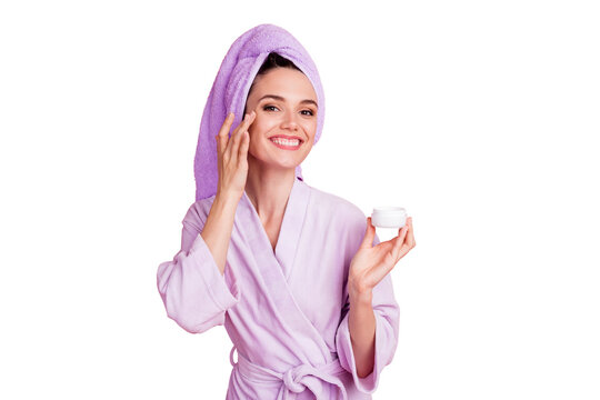 Portrait of lovely cheerful girl wearing towel turban on hair applying day cream on face isolated on pink pastel color background