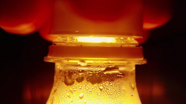 Macro Close Up View of Hand Opening Cool Plastic Water Bottle Cap Highlighted in Yellow Light