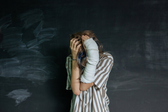 Distressed young woman covering face with bruised arm in cast, concept of domestic violence, emotional abuse, trauma and mental health