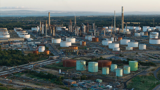 Aerial view of the Fawley Refinery with numerous storage tanks, industrial infrastructure, and pipelines under golden hour light in Southampton, England, United Kingdom.