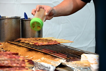 Fototapeta premium Charcoal grilled meat skewers are seasoned with powder by hand at a food stall in Banqiao Christmasland Market, Banqiao District, New Taipei City, Taiwan.