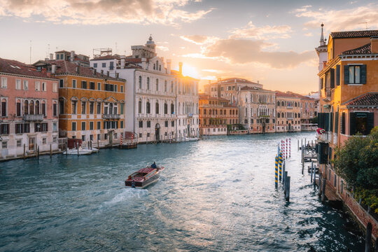 Aerial view of the Grand Canal in Venice at sunset, featuring historic buildings, a water taxi cruising on the water, and warm golden light in Venezia, Veneto, Italy.