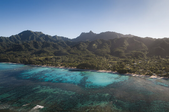 Aerial view of Rarotonga island featuring a vibrant turquoise lagoon, coral reef, lush green mountains, and palm-fringed coastline in the Cook Islands.