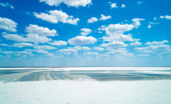 Expansive salt landscape at Baskunchak lake with distinct mining patterns under a bright blue sky and scattered white clouds
