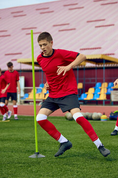Teenage male football player practicing rapid direction change around training poles. Concept of reactive agility, technical footwork, competitive performance.