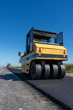 Pneumatic tire roller and asphalt paver machine compacting new road surface on highway