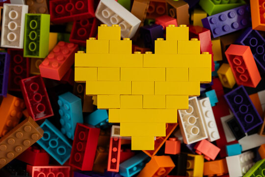 Yellow heart built from Lego bricks on colorful background of Lego pieces