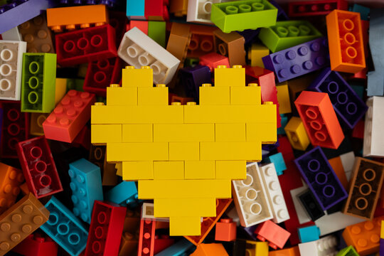Yellow heart built from Lego bricks on colorful background of Lego pieces