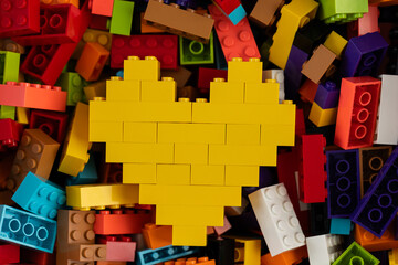 Fototapeta premium Yellow heart built from Lego bricks on colorful background of Lego pieces