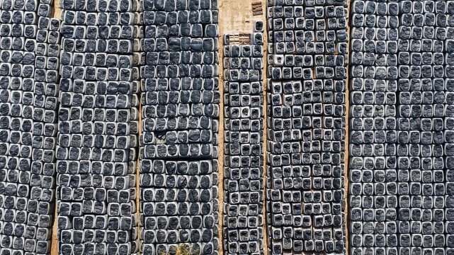 Aerial view of rows of black-wrapped hay bales arranged in a precise grid pattern on a dirt field in Dallas, Texas, United States.