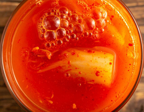 Close up of active bubbles and red chili paste inside a glass kimchi jar showing fermentation texture.