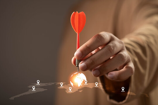 Close-up of a hand placing a red dart on a global map, symbolizing business strategy, global targeting, market expansion, international growth, location planning, and worldwide success.