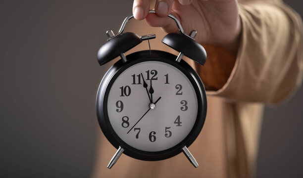 Hand holding alarm clock symbolizing time management, productivity, punctuality and deadline planning. Modern business concept representing efficiency, scheduling and work organization.
