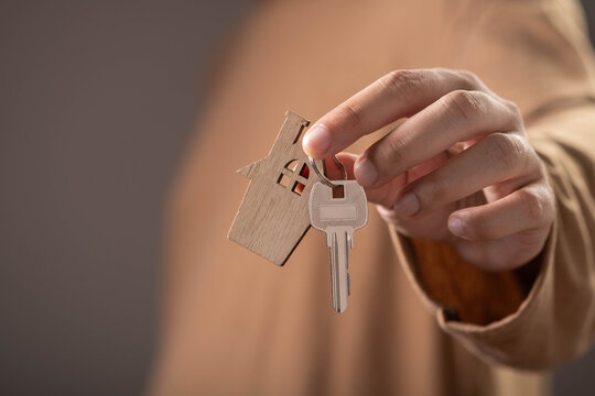 Hand holding house key with home-shaped keychain, symbolizing homeownership, real estate investment, property purchase, mortgage approval, residential housing, and moving into a new home.