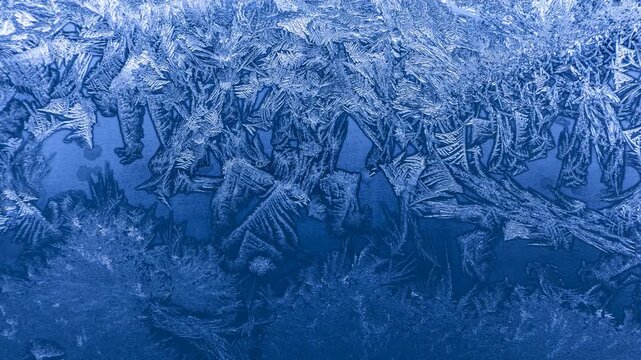 Frost crystal patterns forming intricate geometric shapes on glass in extreme winter cold

