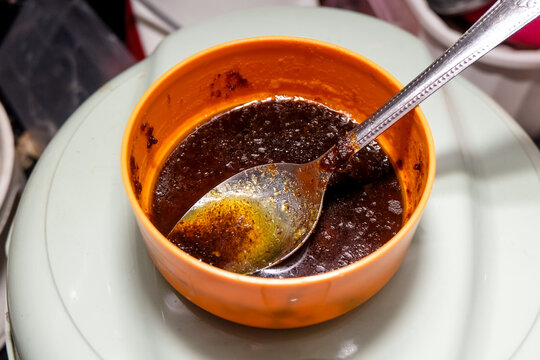 ark savory chili sauce resting in a small orange plastic bowl with a metal spoon inside.