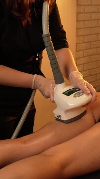 Vacuum roller massage. Anti-cellulite stage. Dim atmospheric warm light. Masseuse massages a woman's leg and thighs with a device. self-care, care, weight loss. slow motion