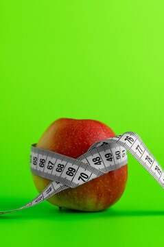 Fresh red apple wrapped with a measuring tape on a green background, weight loss concept