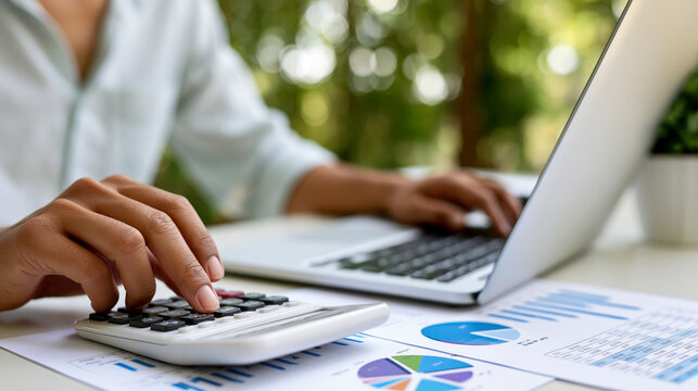 Faceless young analyst cross-referencing financial reports with a calculator and laptop, financial reports, calculator, laptop technology, business analytics, data verification,