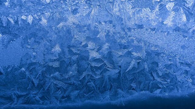 Frost crystal patterns forming intricate geometric shapes on glass in extreme winter cold
