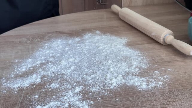 Close up of sprinkling flour onto wooden table before rolling dough for homemade apple strudel