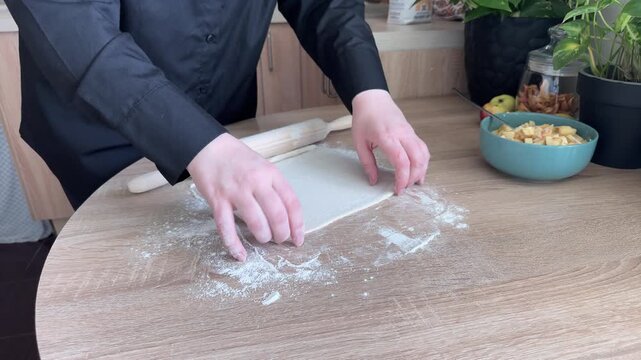 Rolling out puff pastry on floured wooden table for homemade apple strudel