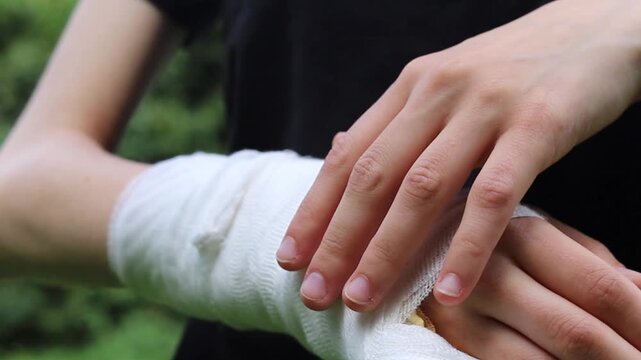 Hand gently checks white gauze wrap on a sore wrist to provide support and comfort outdoors during the day while helping with the healing process after a recent minor injury to the joint area